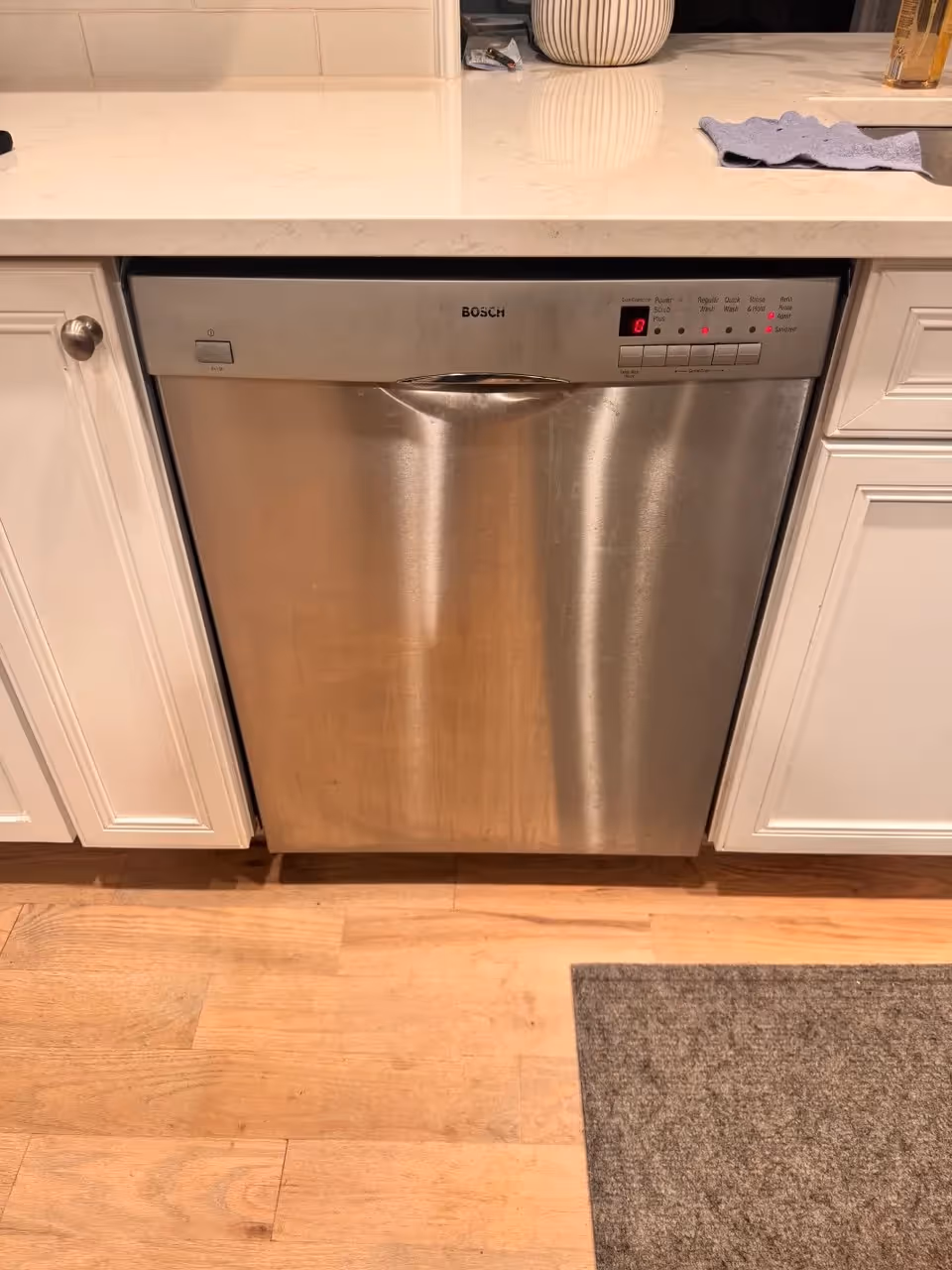Bosch stainless steel dishwasher with control panel mounted under white countertop.