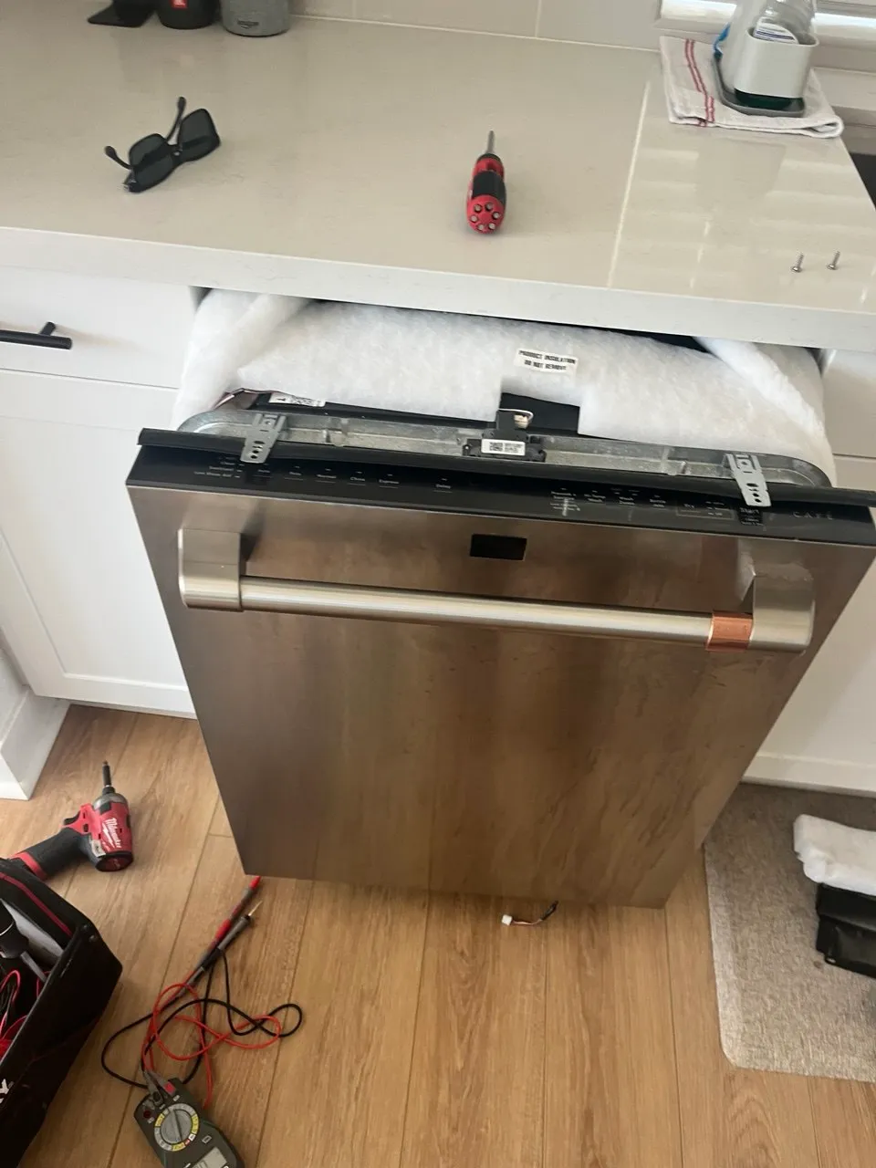 Stainless steel GE dishwasher partially pulled out for repair with tools on the floor.
