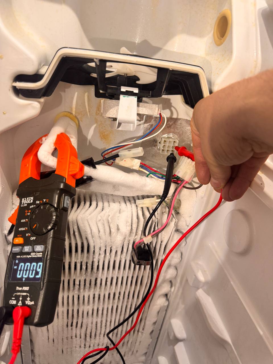 Technician testing defrost heater circuit on a frosted evaporator coil inside a built-in refrigerator
