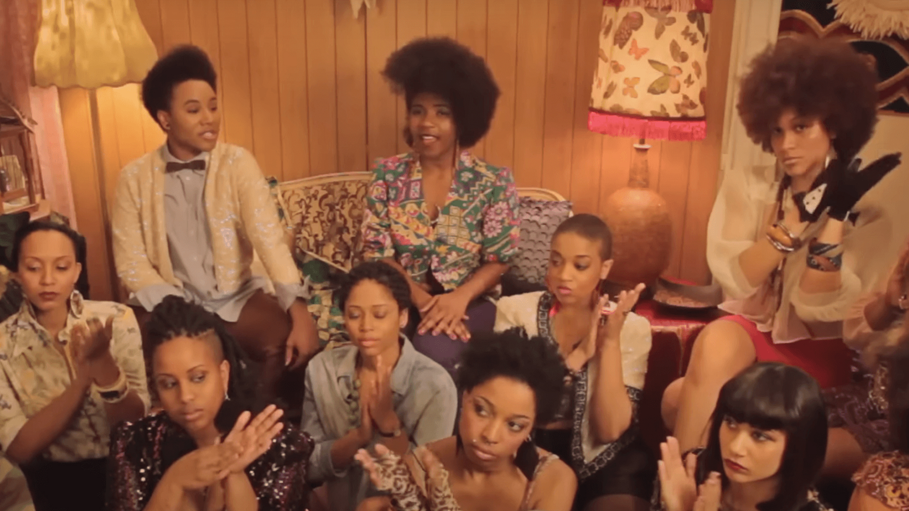 Screenshot from THEESatisfaction’s music video "Queens," featuring a group of women sitting together, clapping hands in rhythm.