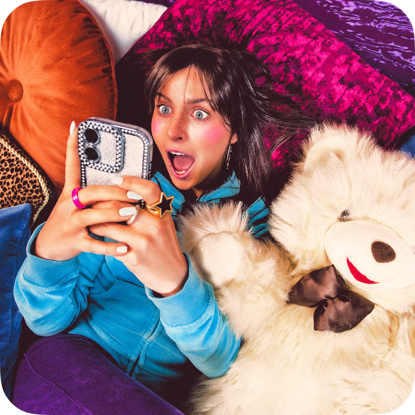Jeune femme surprise regardant son smartphone, allongée près d'un ours en peluche