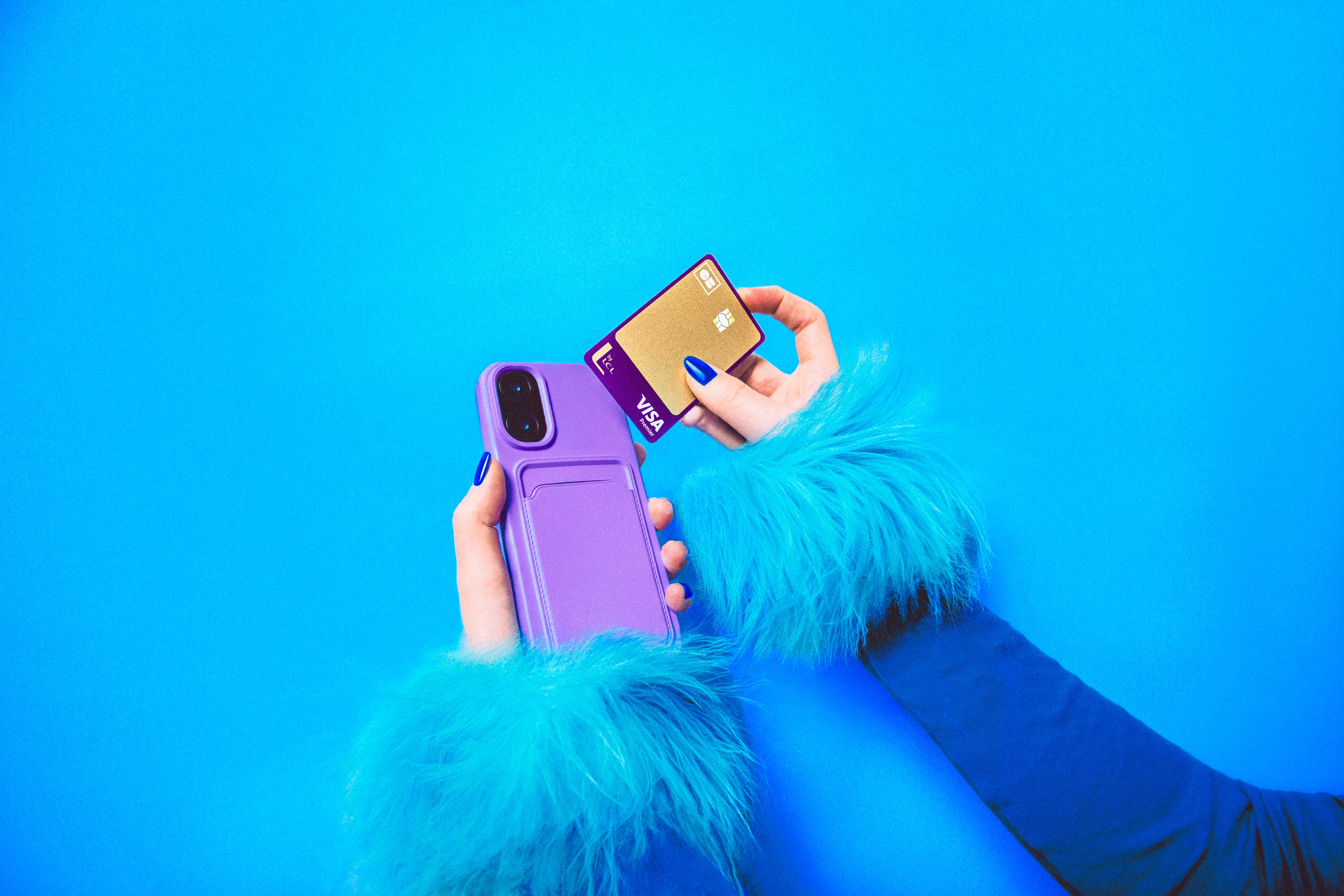 Main tenant une carte CB Visa Premier dorée et un téléphone violet