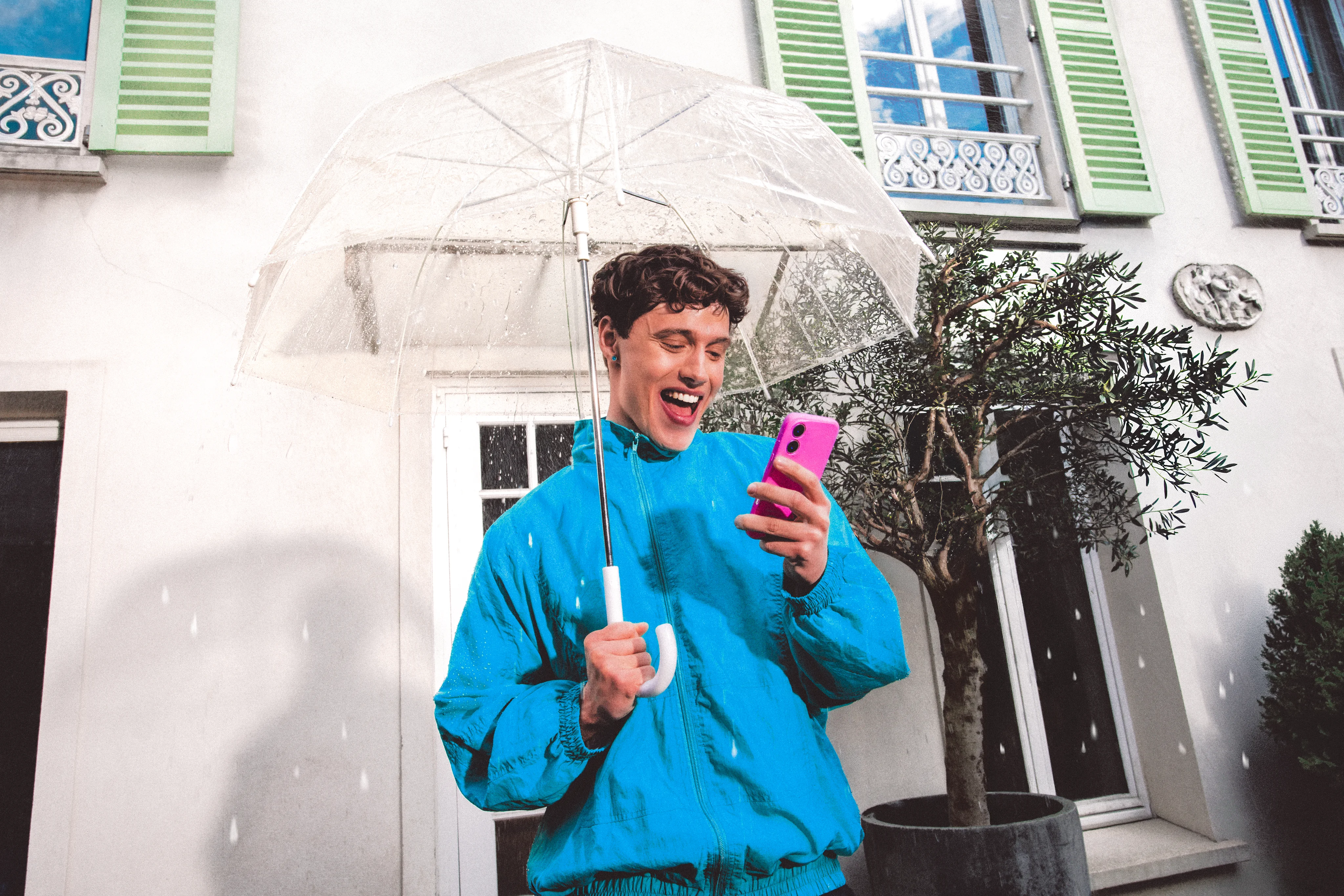 Homme en veste bleue avec un parapluie transparent tenant un téléphone rose