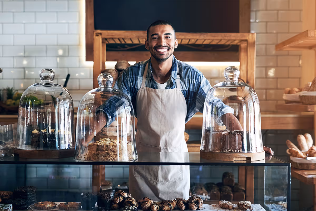 A bakery owner is smiling behind a counter full of baked treats.