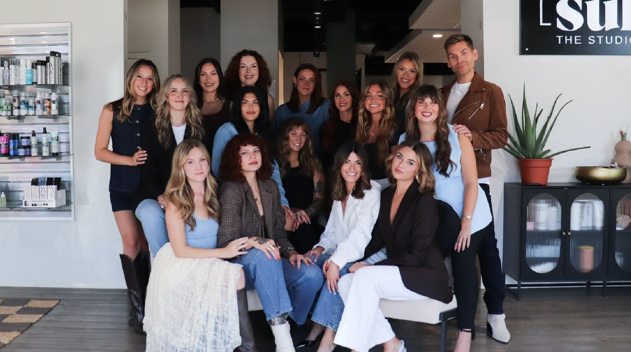The staff at Sul The Studio in Grand Rapids Michigan posing indoors in a modern studio with shelves of beauty products and a plant nearby.