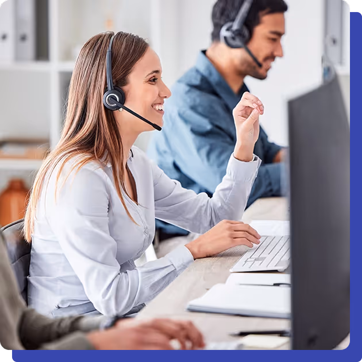 Smiling customer service representative wearing a headset and working on a computer in a modern office.