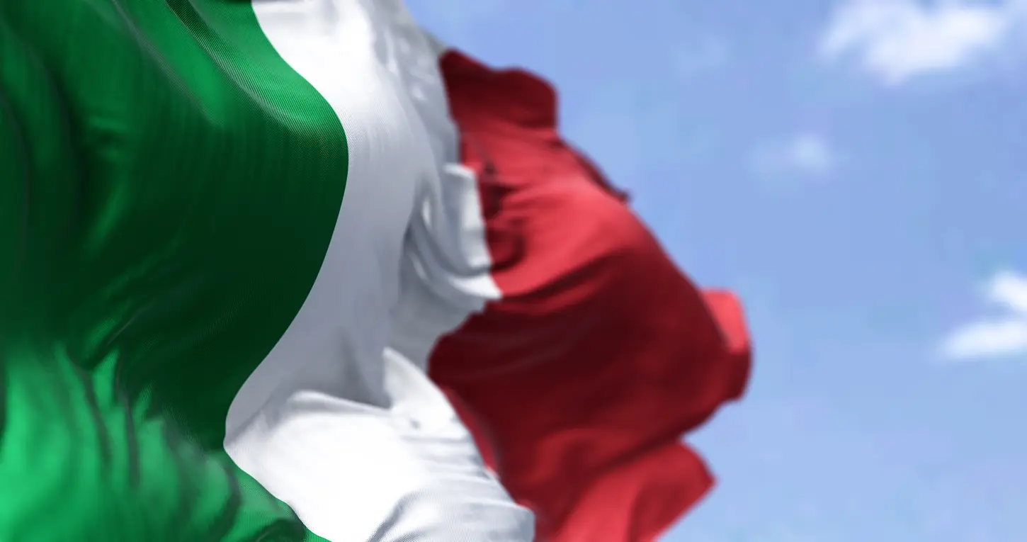 Close-up of the Italian flag waving against a partly cloudy blue sky.