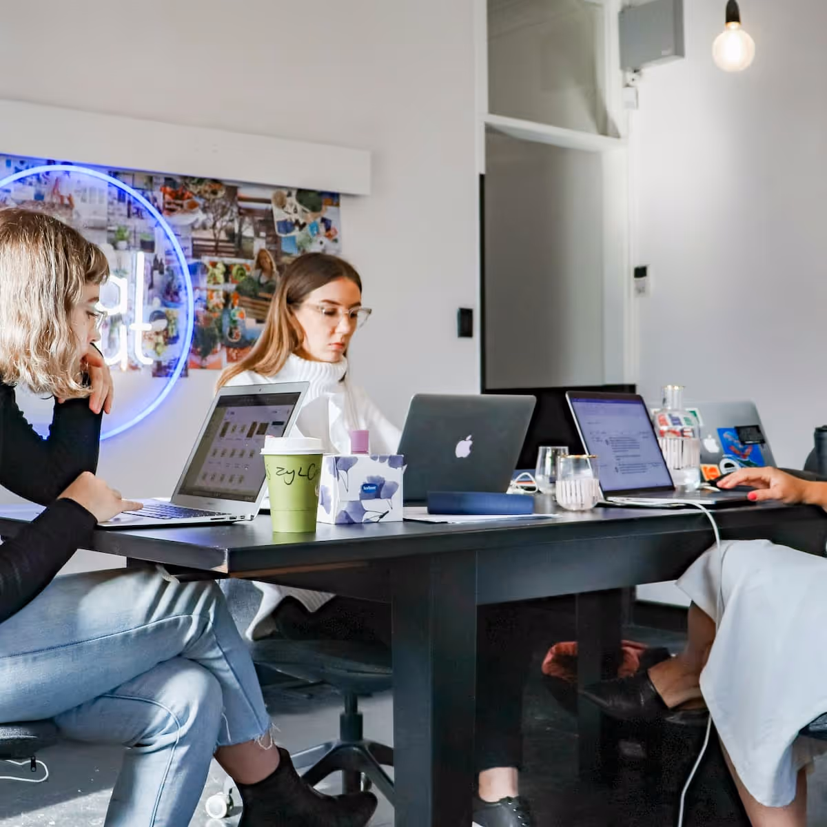 Trois personnes assises autour d'une table de travail avec des ordinateurs portables, dans un bureau moderne lumineux.