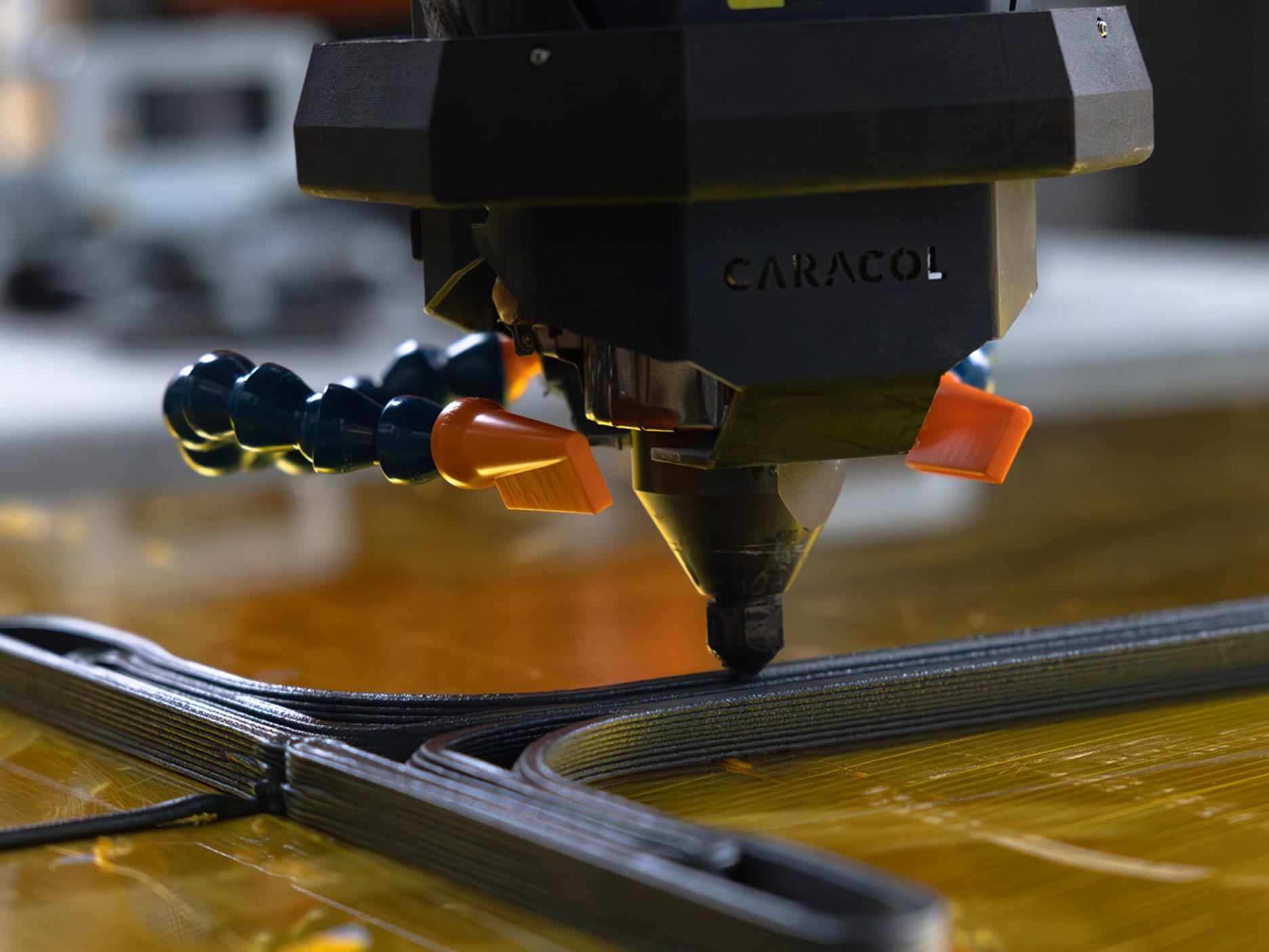 Close-up of a 3D printer nozzle extruding black filament in layers on a yellow base.