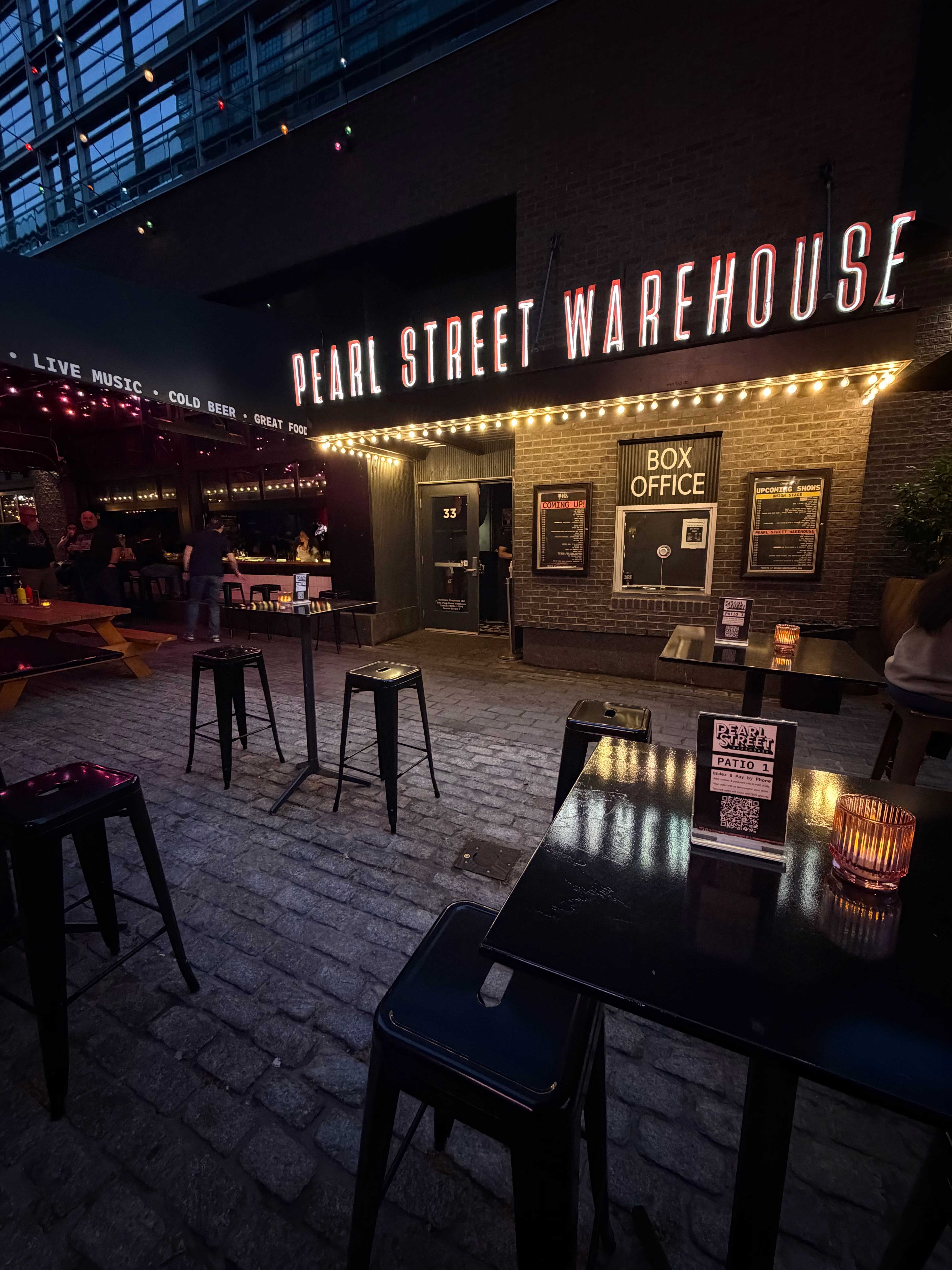 Pearl Street Warehouse patio with high-top tables outside the box office at night
