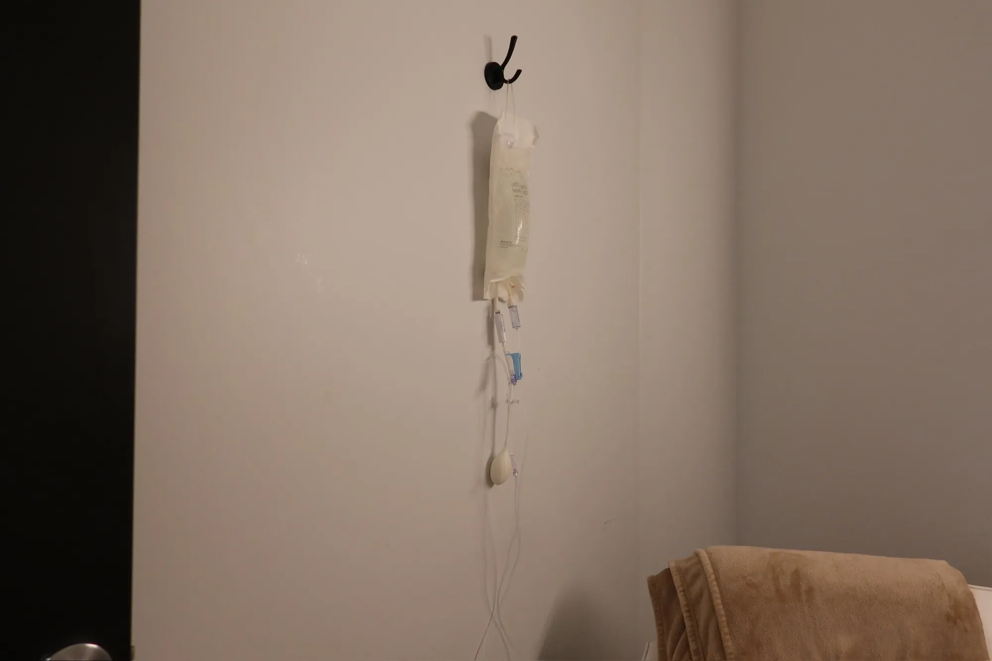 IV bag hanging from a wall hook beside a blanket-draped lounge chair.