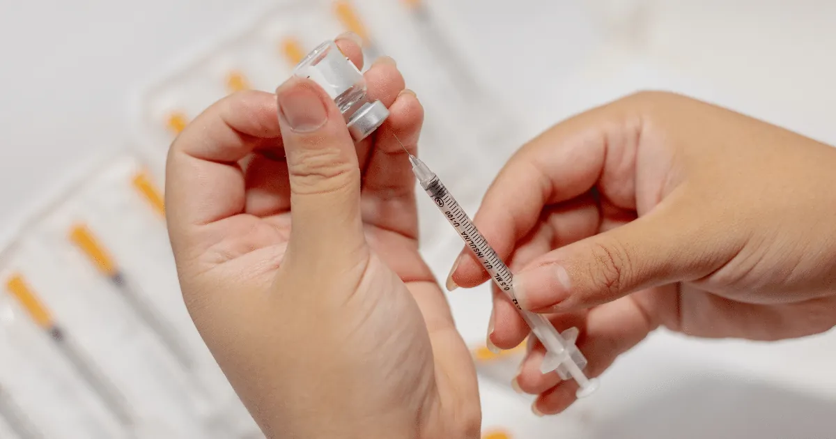 Hands drawing medication from a small vial into a syringe.