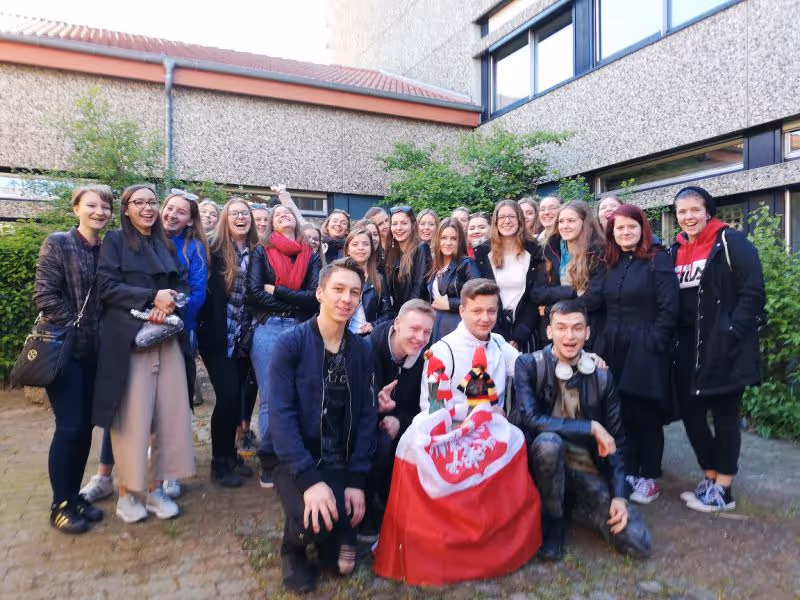 Eine große Gruppe von jungen Erwachsenen posiert lachend vor einem Gebäude im Freien.