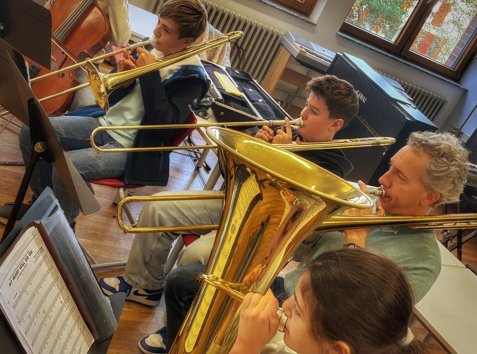 Vier Musiker, drei mit Posaunen und eine mit Tuba, spielen zusammen in einem hellen Raum mit Fenstern.