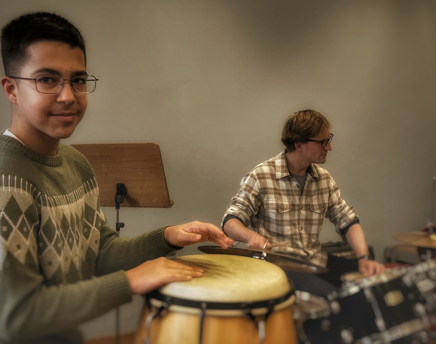 Zwei junge Männer spielen gemeinsam in einem Raum Schlaginstrumente, einer auf der Conga, der andere am Schlagzeug.