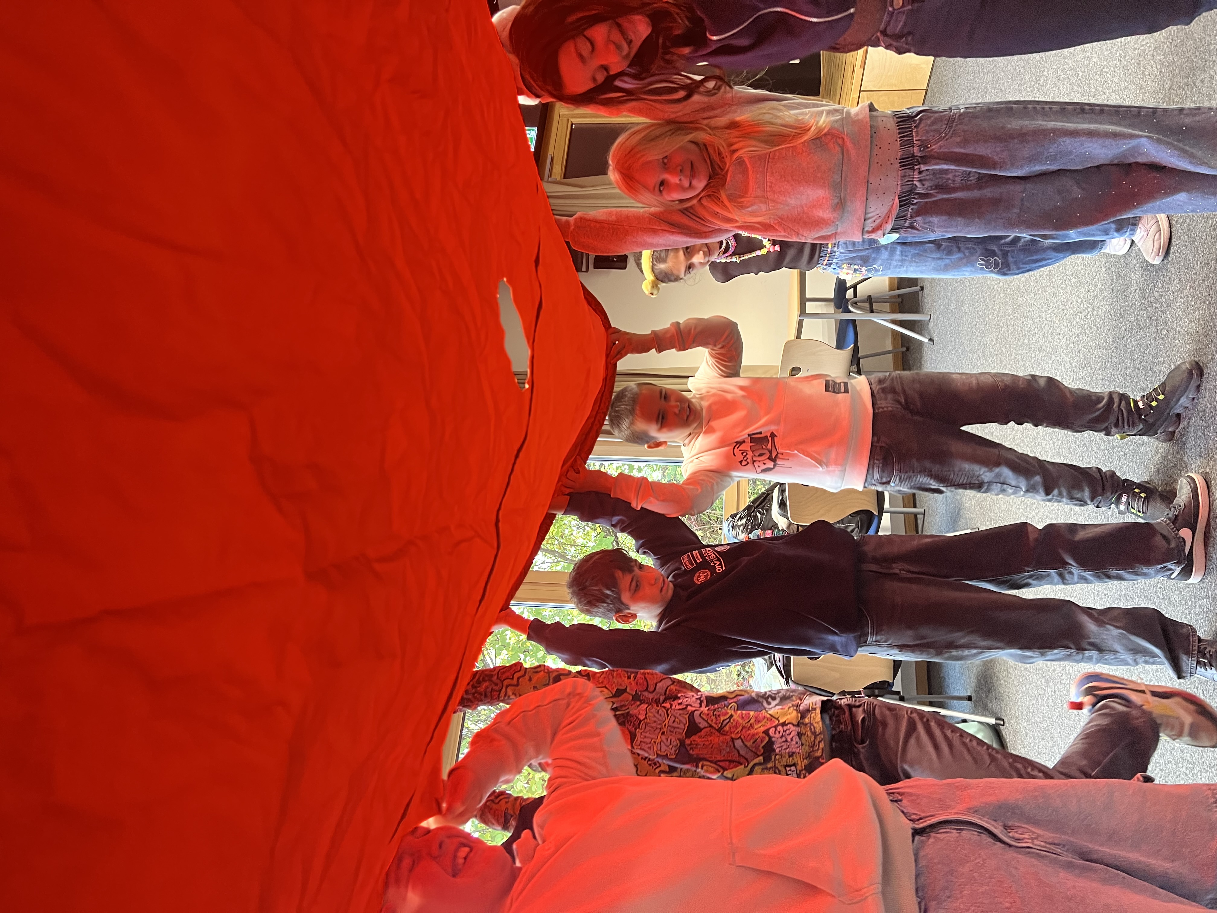 Kinder stehen in einem Kreis und halten ein großes rotes Tuch über sich.