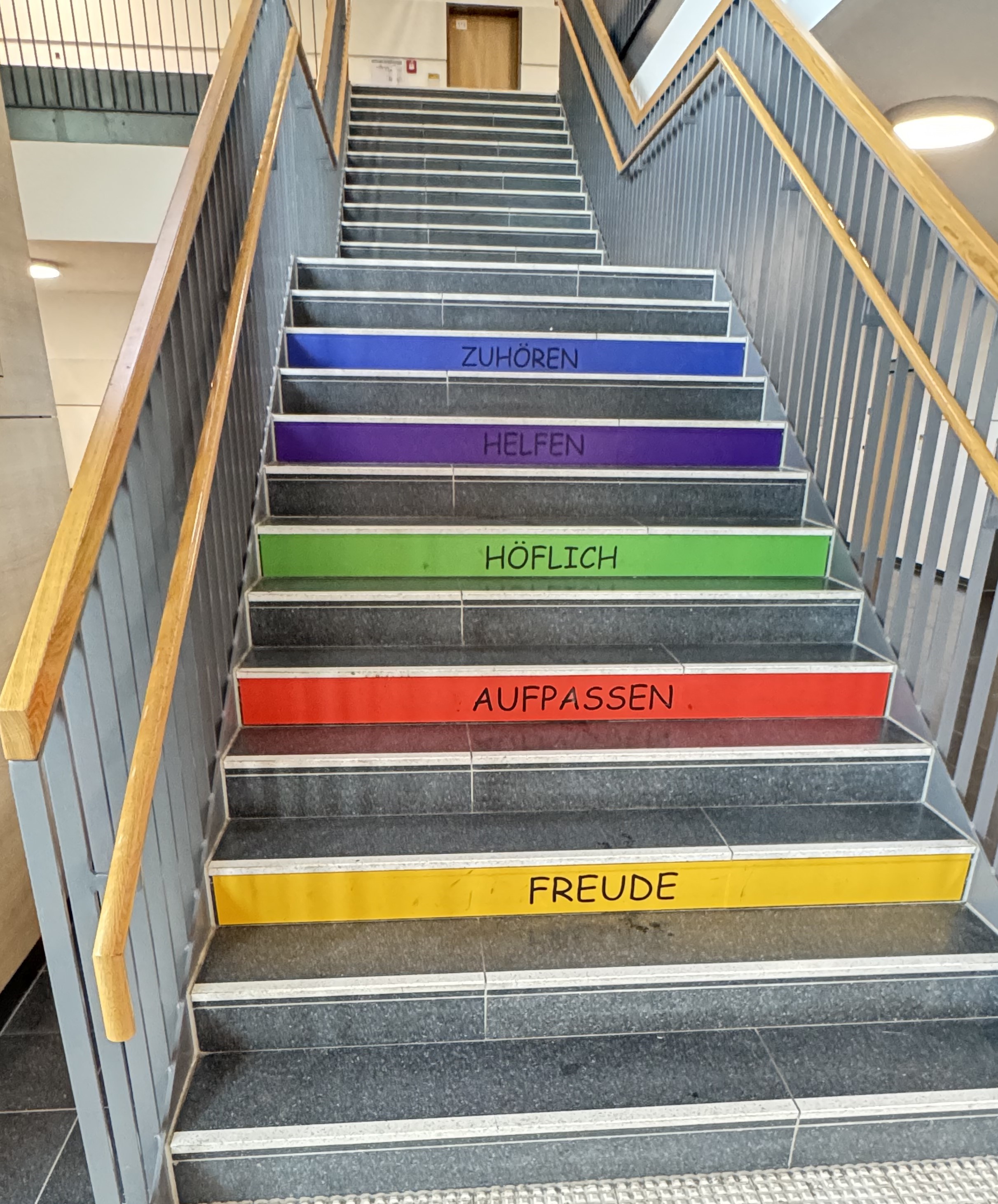 Treppenstufen mit bunten Streifen und den Worten Zuhören, Helfen, Höflich, Aufpassen, Freude.