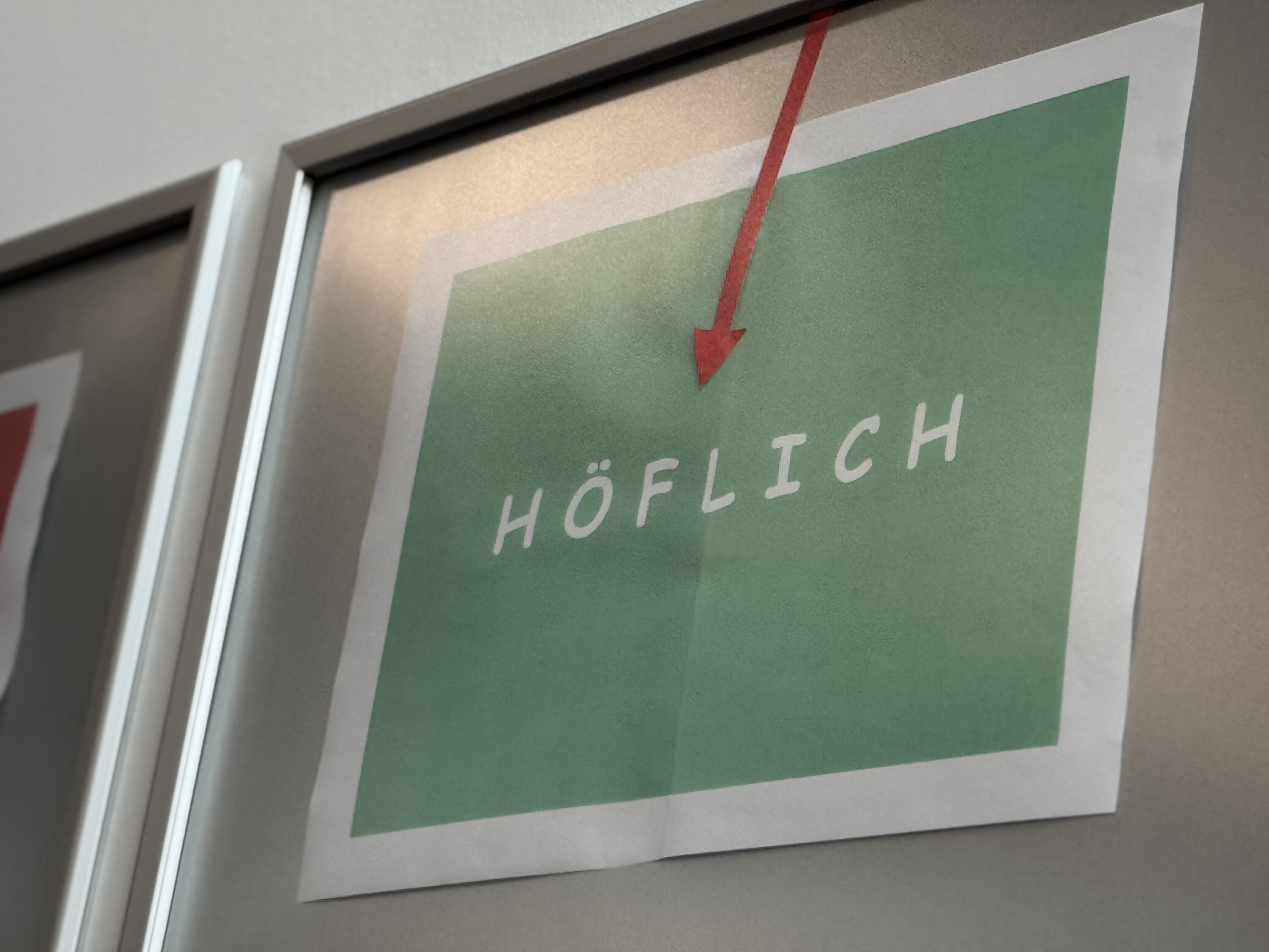 Grünes Schild mit dem Wort "HÖFLICH" und einem roten Pfeil darauf.