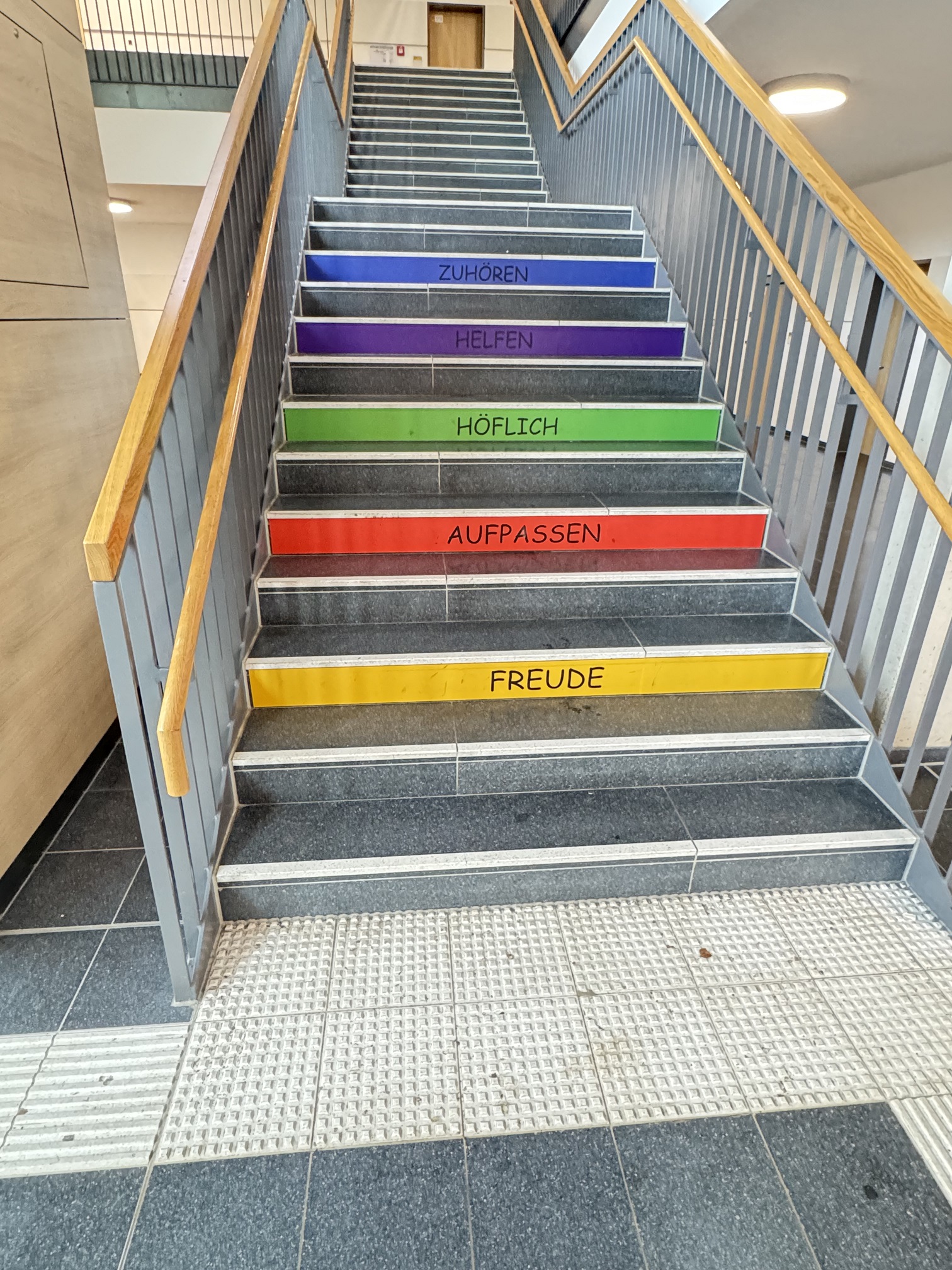 Treppenhaus mit farbigen Stufenbeschriftungen: Freude, Aufpassen, Höflich, Helfen, Zuhören.