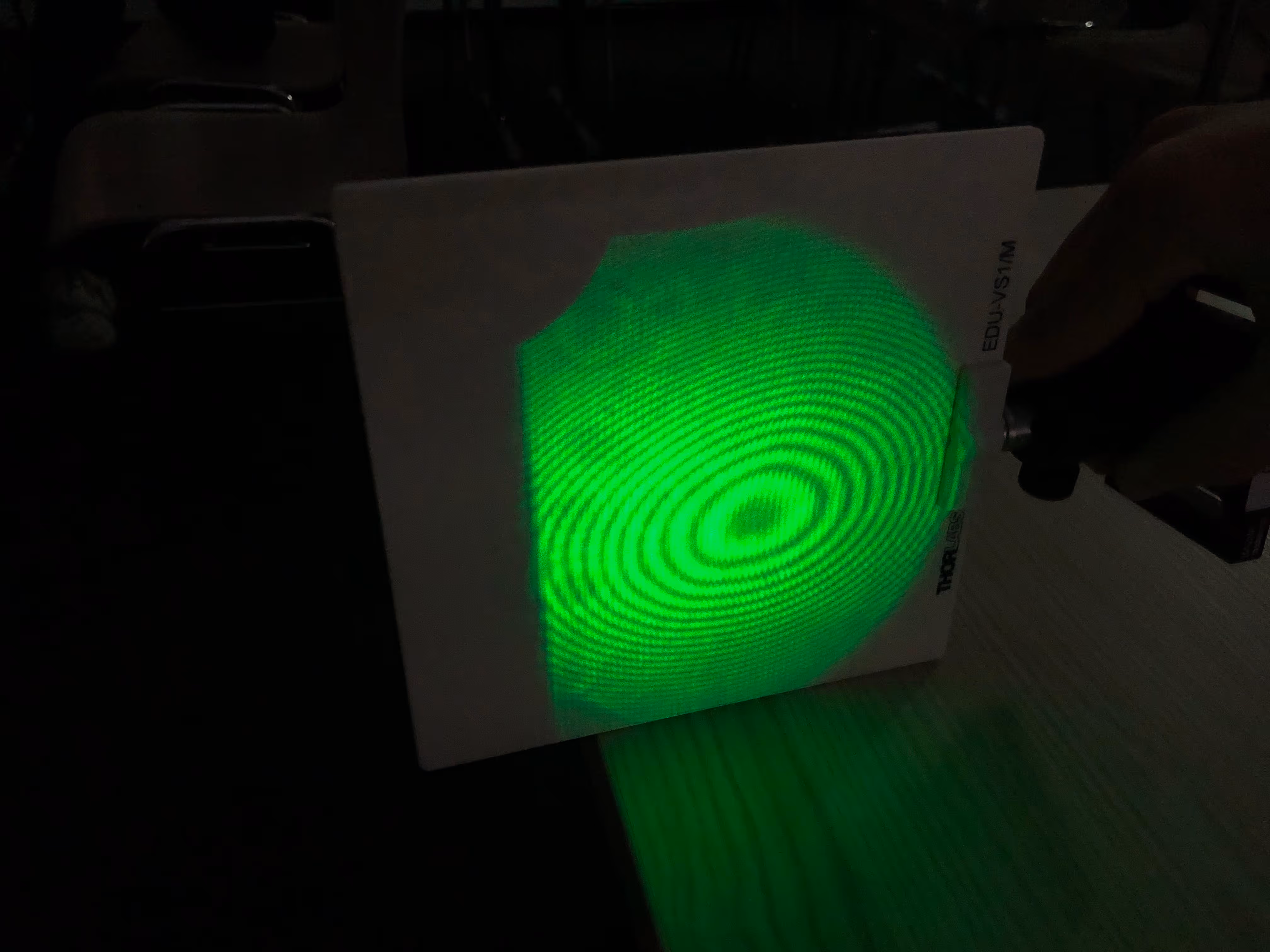 Bei einem physikalischen Experiment sieht man grünes Licht auf einem schwarzen Schirm strahlen