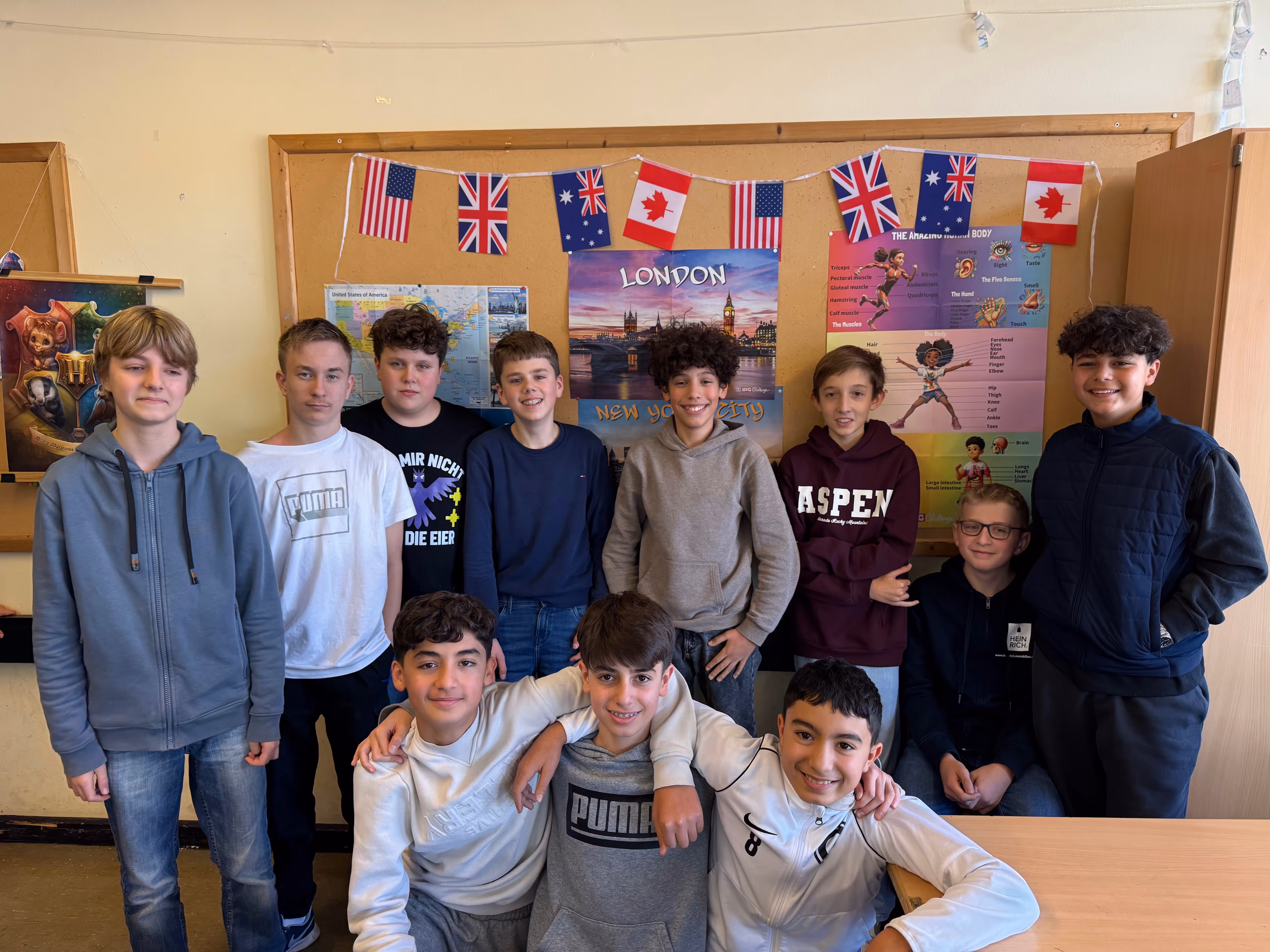 11 Schüler posieren im Klassenzimmer vor den Flaggen englischsprachiger Länder und Postern von New York und London.