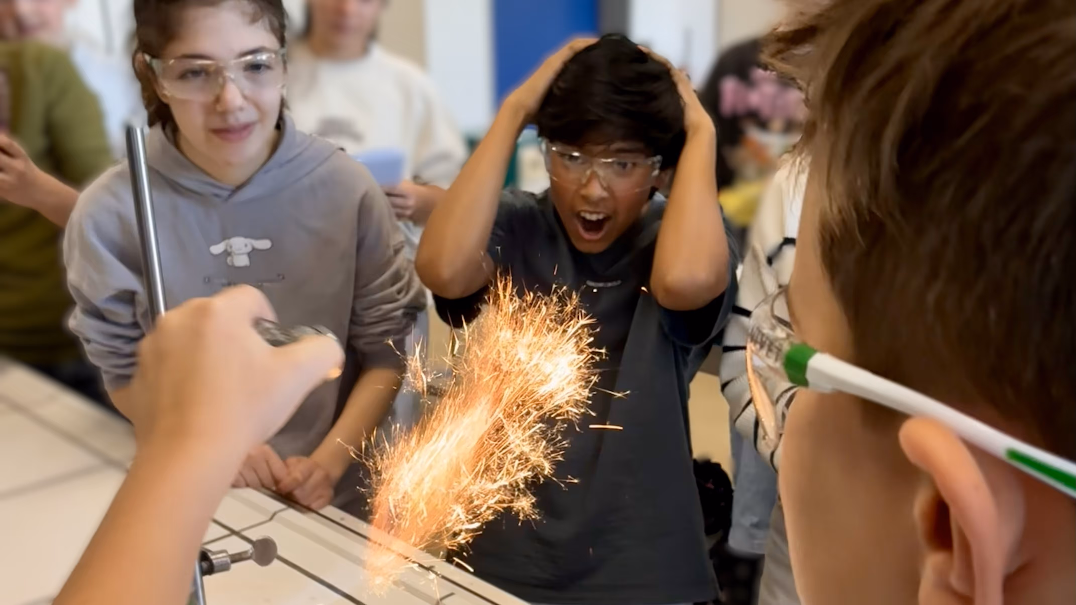 Ein Schüler führt ein Experiment durch, bei dem Funken entstehen, was zwei weitere Schüler begeistert beobachten.
