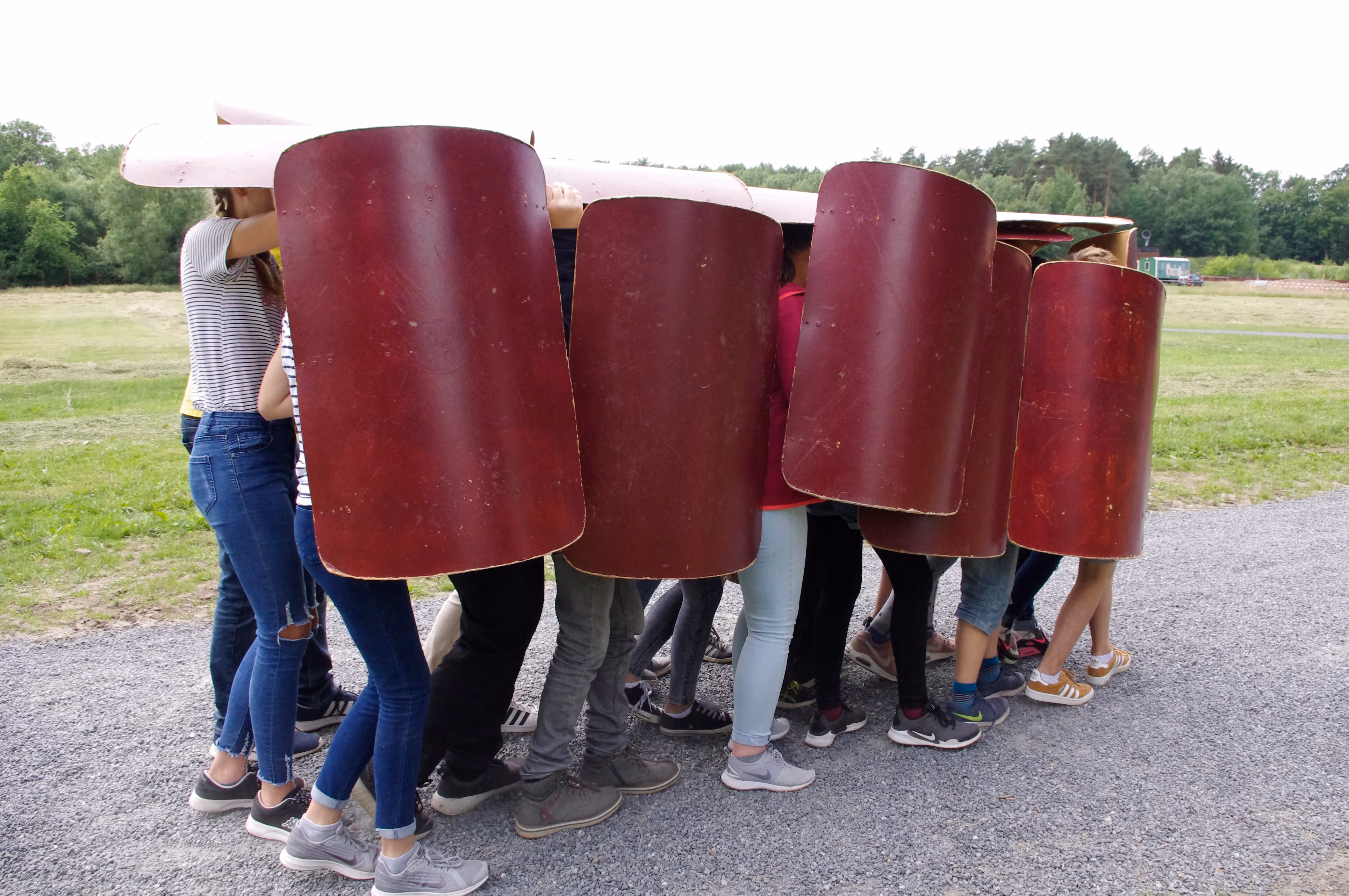 Schüler:innen verstecken sich hinter römischen Schildern in Karlkriese.