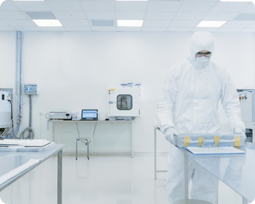 Personne en combinaison de protection blanche dans un laboratoire propre manipulant un équipement sur une table en acier inoxydable.