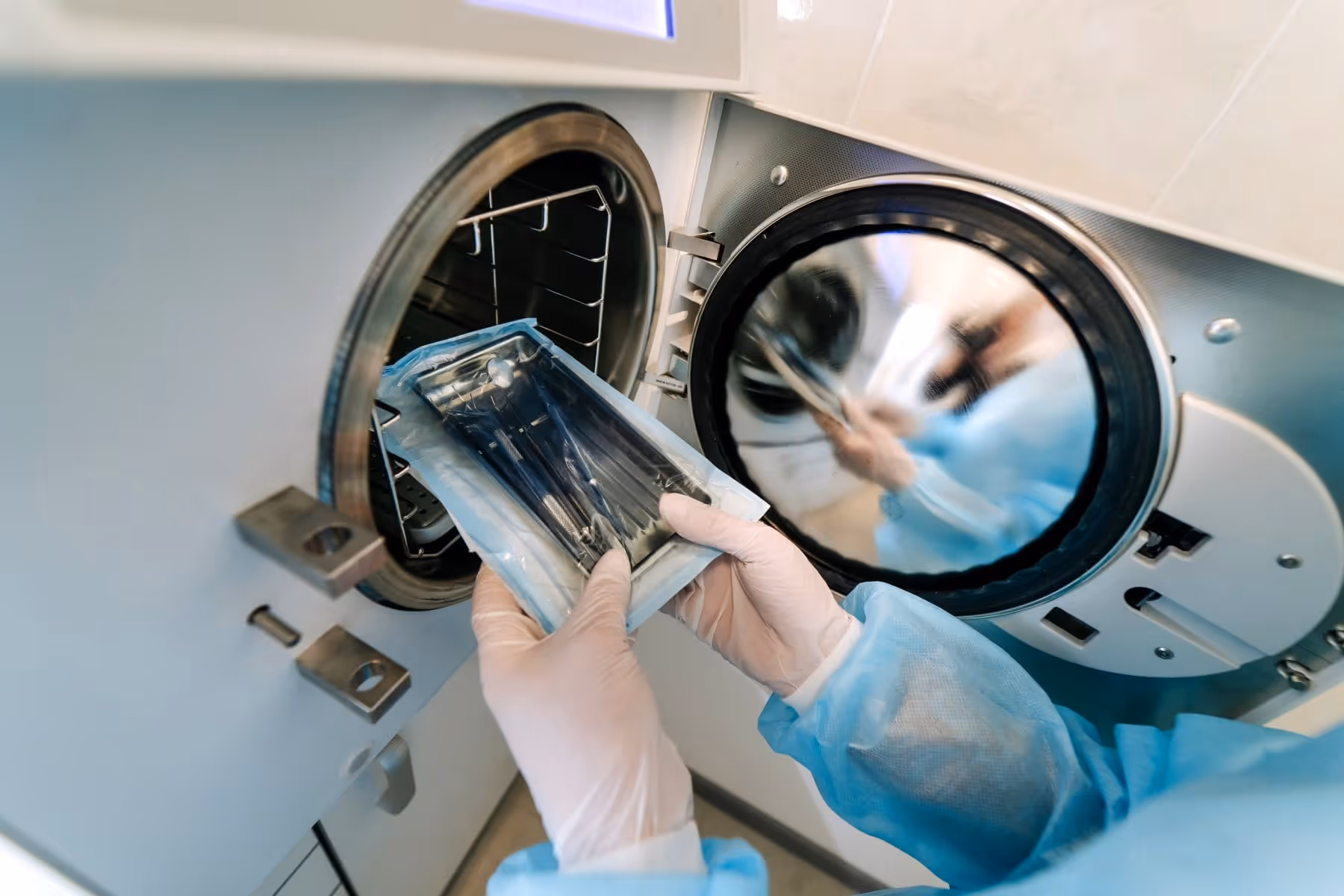 Une personne portant des gants et une blouse bleue retire un paquet d'instruments stériles d'un autoclave.
