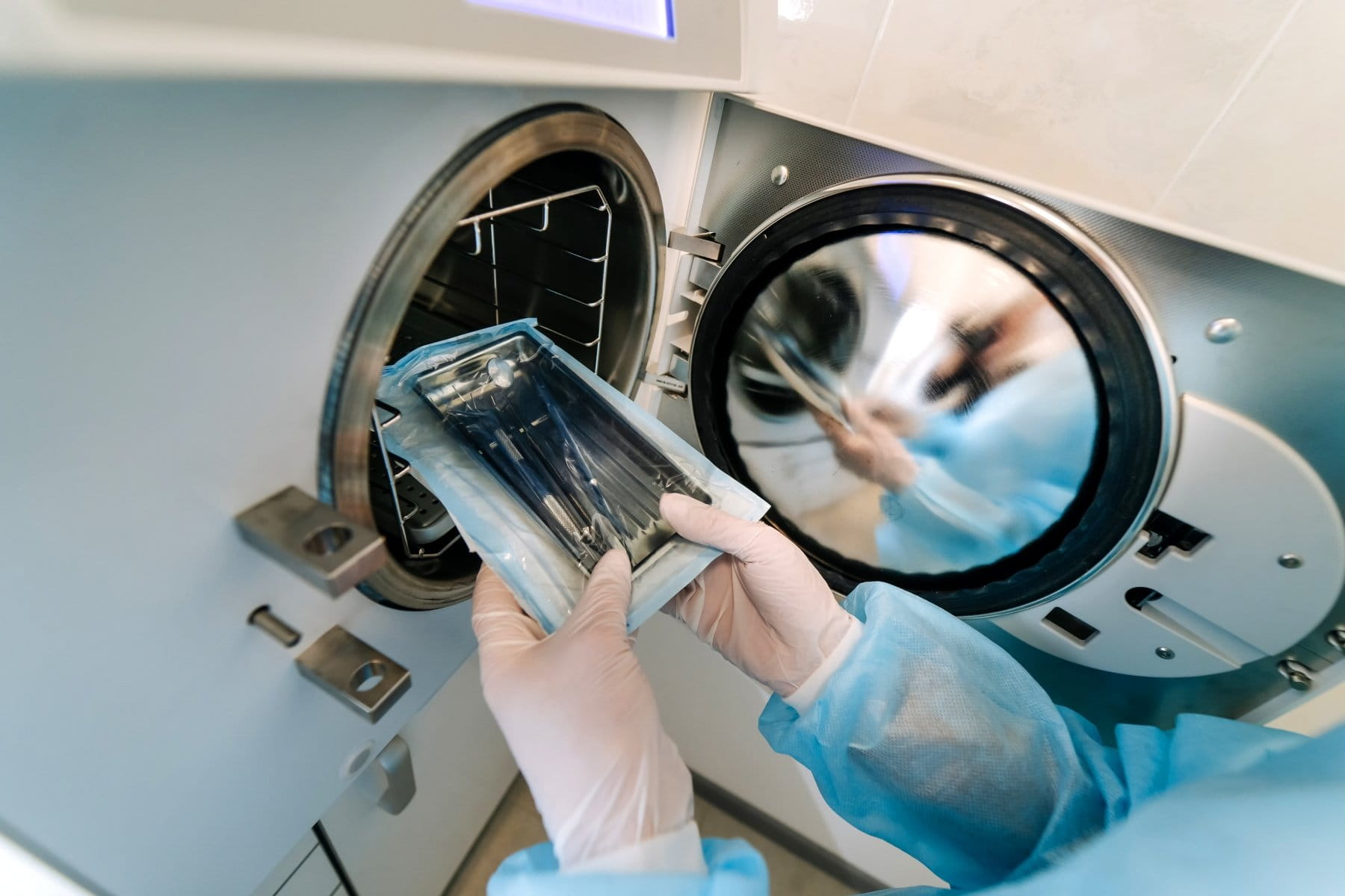 Une personne portant des gants et une blouse bleue retire un paquet d'instruments stériles d'un autoclave.