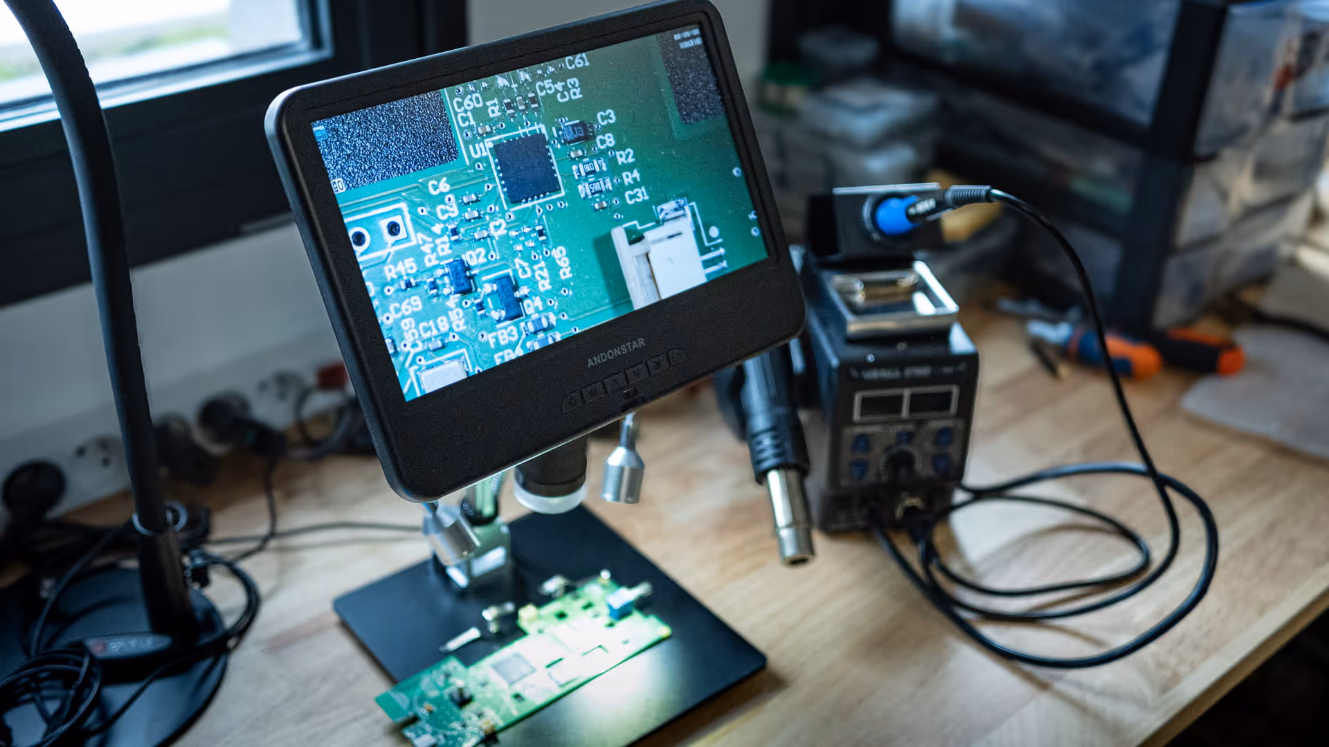 Un microscope numérique montre une carte de circuit imprimé détaillée, avec un équipement de soudure en arrière-plan sur une table en bois.