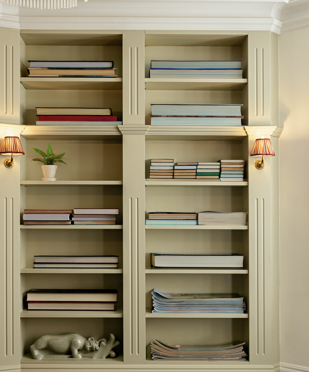 Cream-coloured bookshelf with books, magazines, a plant, and a rhino-shaped sculpture on shelves.