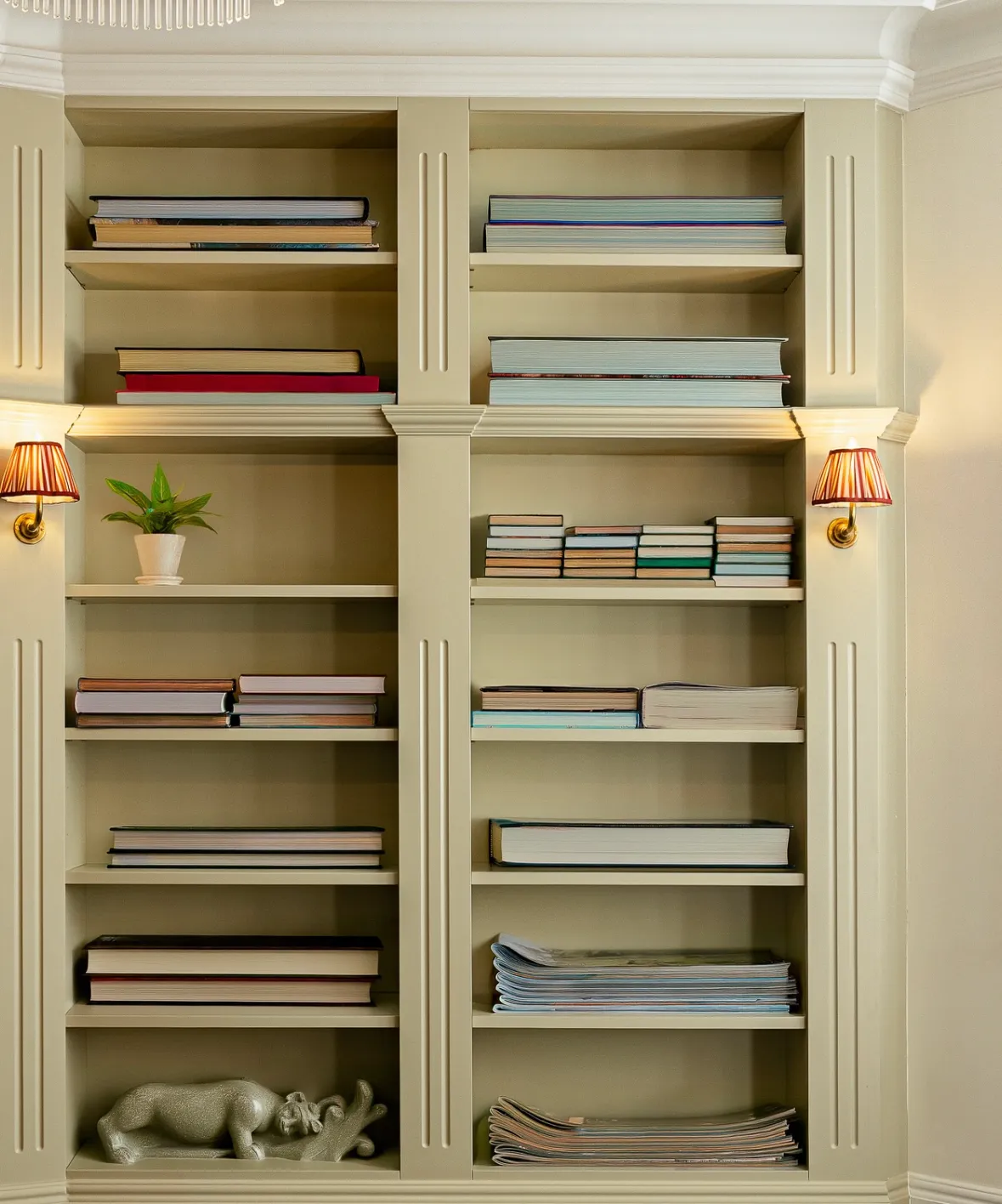 Cream-coloured bookshelf with books, magazines, a plant, and a rhino-shaped sculpture on shelves.