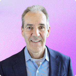 Portrait of a middle-aged man with gray hair wearing a blue checkered shirt and dark blazer, smiling against a purple background.