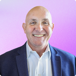 Smiling bald man wearing a navy blazer and white shirt against a purple gradient background.