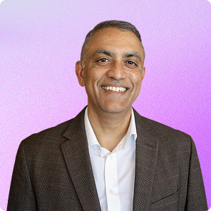 Smiling man wearing a brown suit jacket and white shirt against a purple gradient background.
