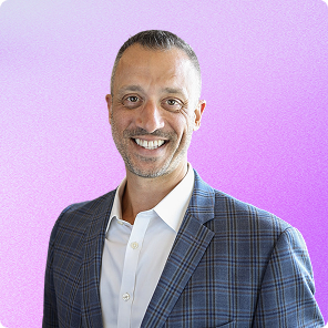 Smiling man wearing a blue checkered blazer and white shirt against a purple gradient background.