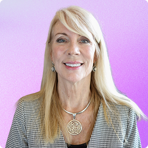 Smiling older blonde woman wearing a checkered jacket and a round pendant necklace on a purple gradient background.