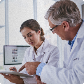 A male and female doctor discussing notes on a clipboard in a medical office.