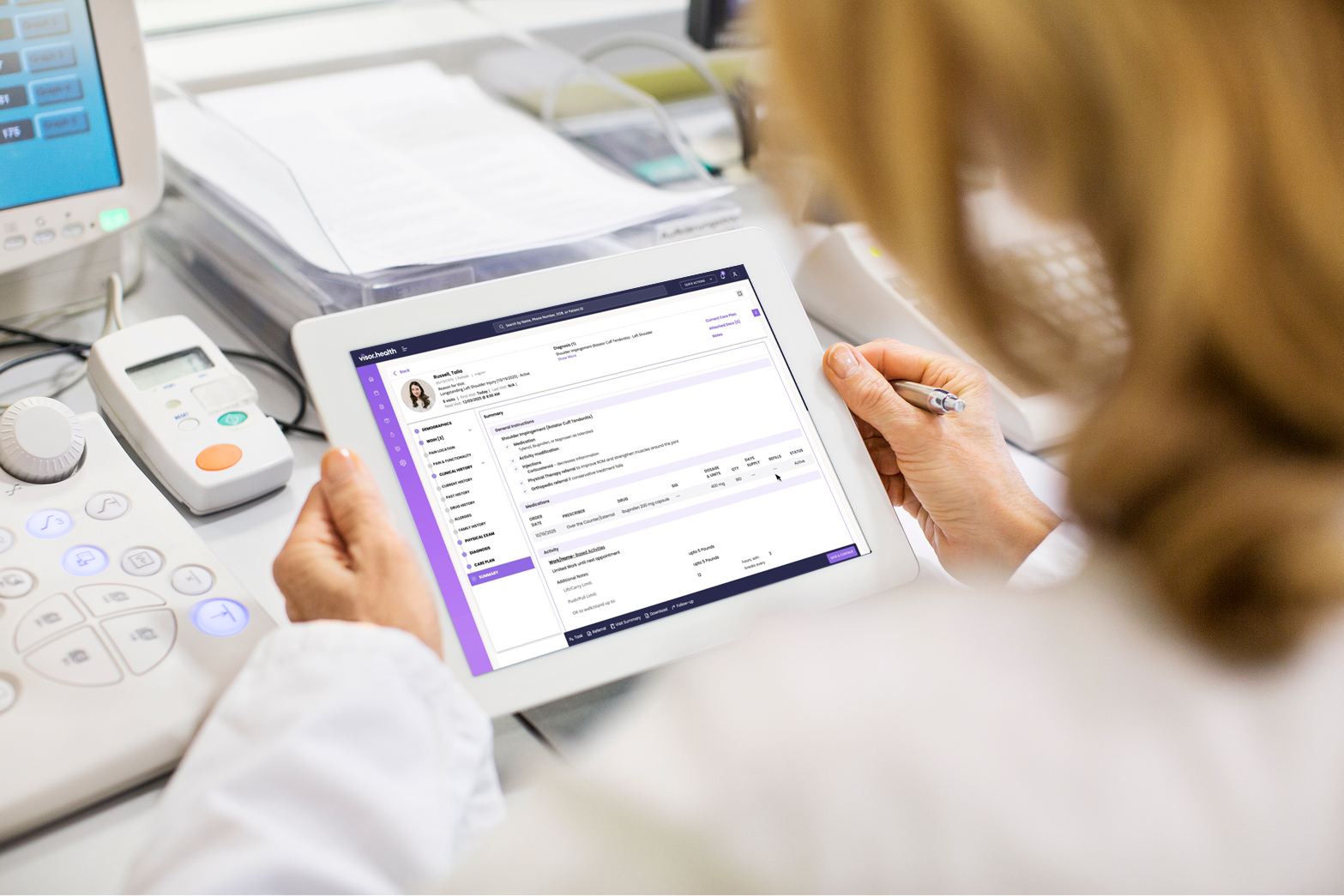 Healthcare professional holding a tablet displaying a patient’s medical record on Vinehealth software in a clinical setting.