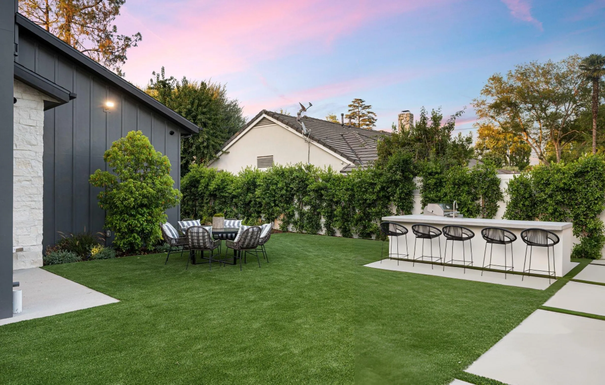 Modern backyard outdoor living space with artificial turf, dining area, and built-in bar