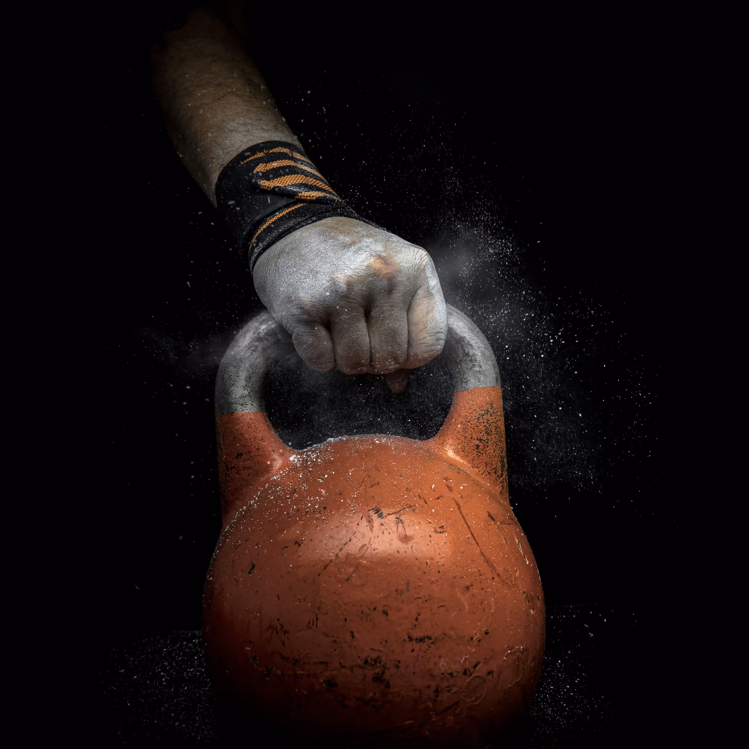 Main avec support de poignet tenant une kettlebell couverte de craie sur fond sombre – exercice de musculation et de force – Coach Getfit Québec.