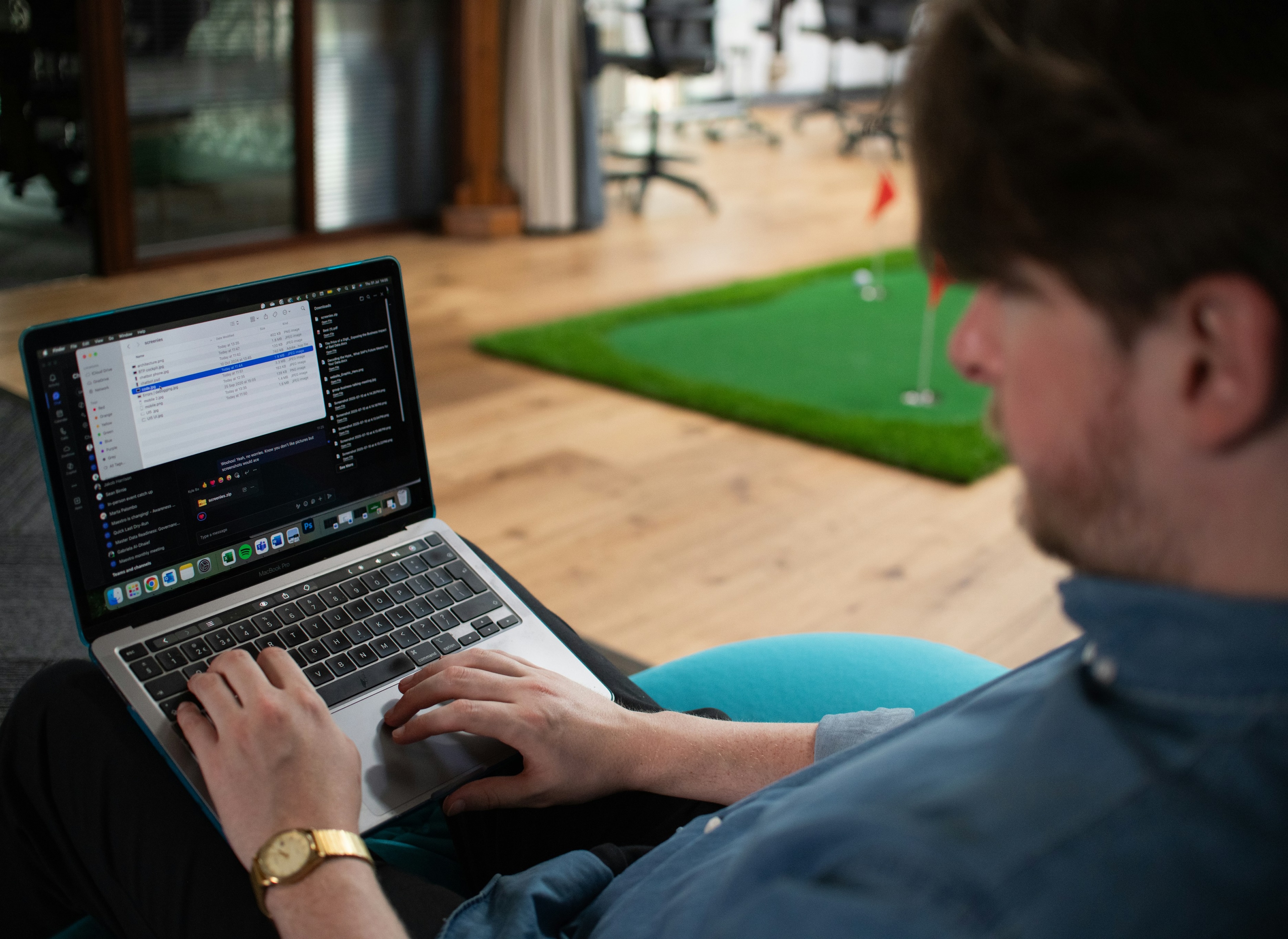 Person using a laptop in a modern workspace with an indoor putting green in the background.