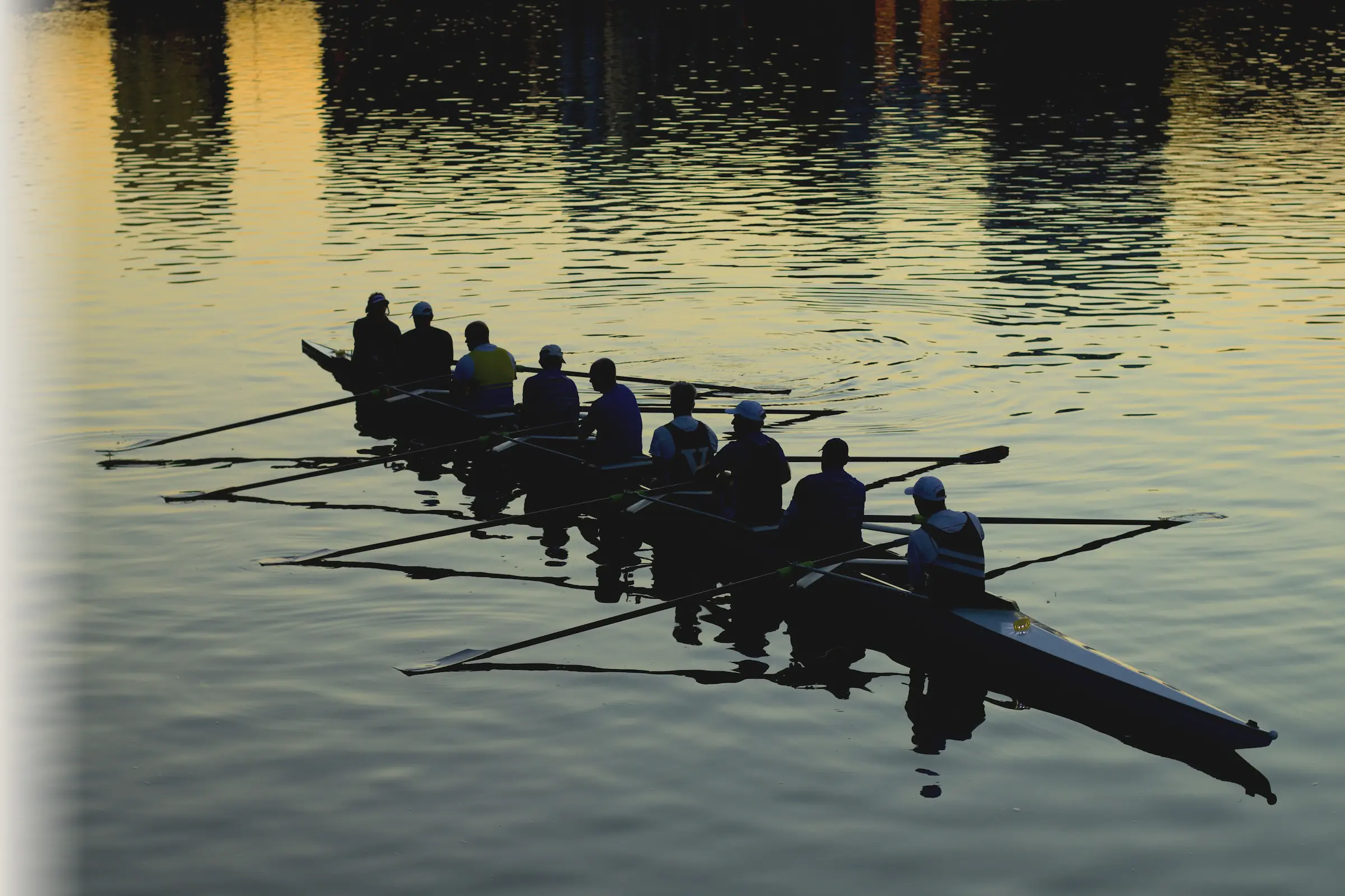 Eight rowers in a boat rowing on calm water at sunset with reflections.
