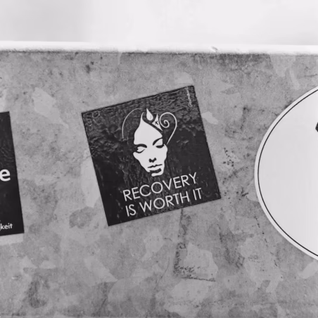 Sticker with an illustrated face wearing a nurse's hat and the text 'RECOVERY IS WORTH IT' on a textured surface.