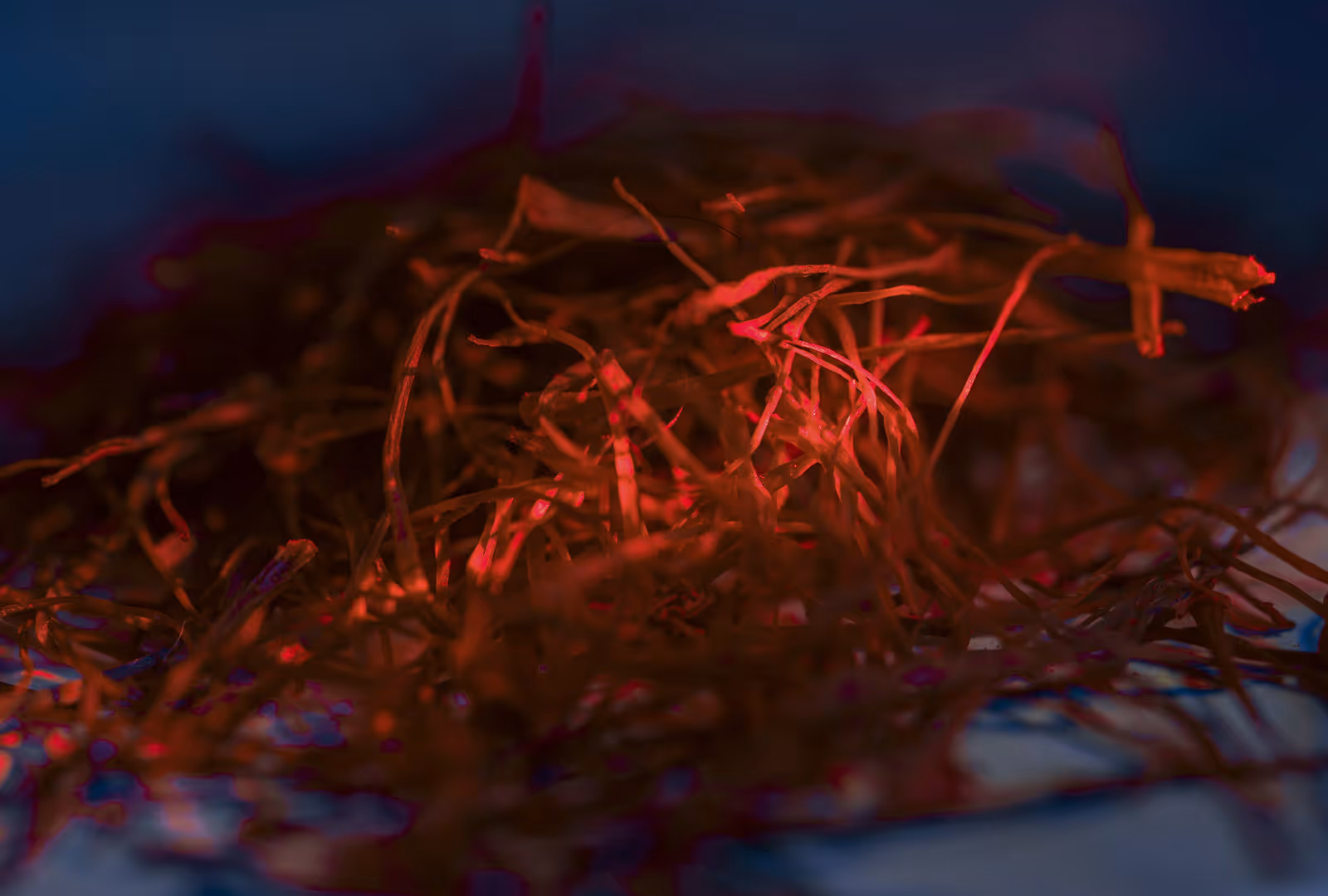 Close-up of thin red threads or strands scattered on a surface with dark background.