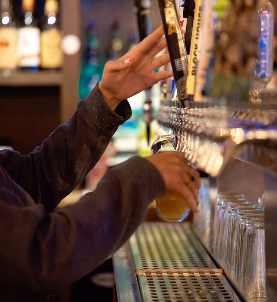 Person pouring a draft beer from a tap at a bar with glassware neatly arranged below.