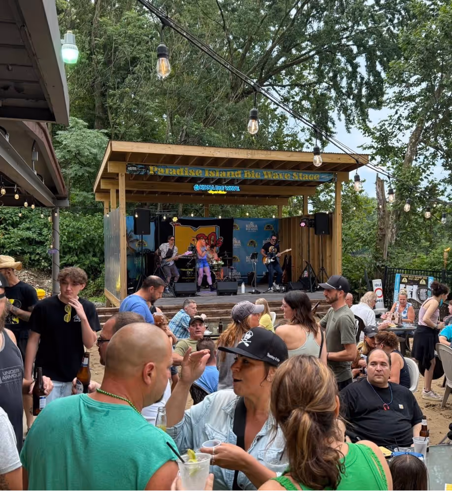Outdoor music event with a band performing on the Paradise Island Big Wave Stage and a crowd socializing under string lights.