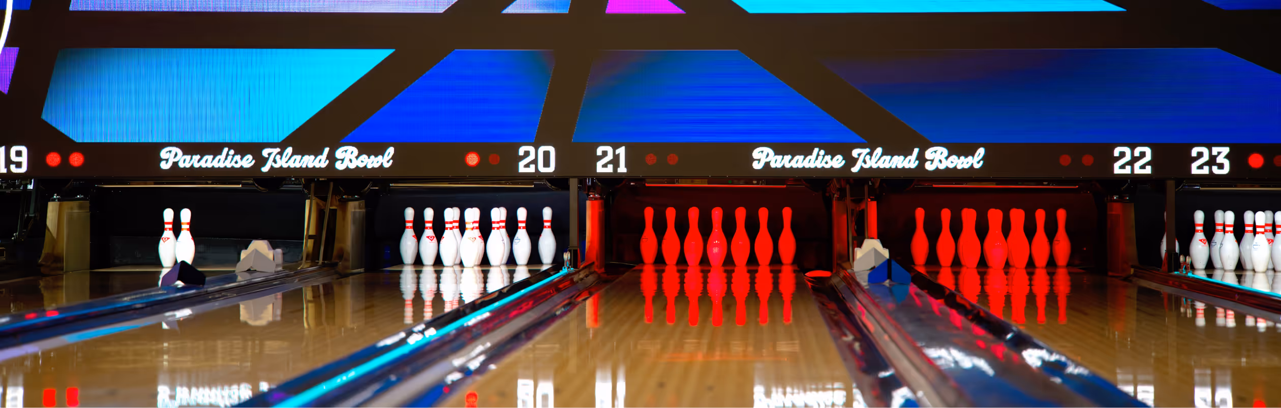 Bowling lanes with pins set up and colorful display screens showing lane numbers and Paradise Island Bowl text.