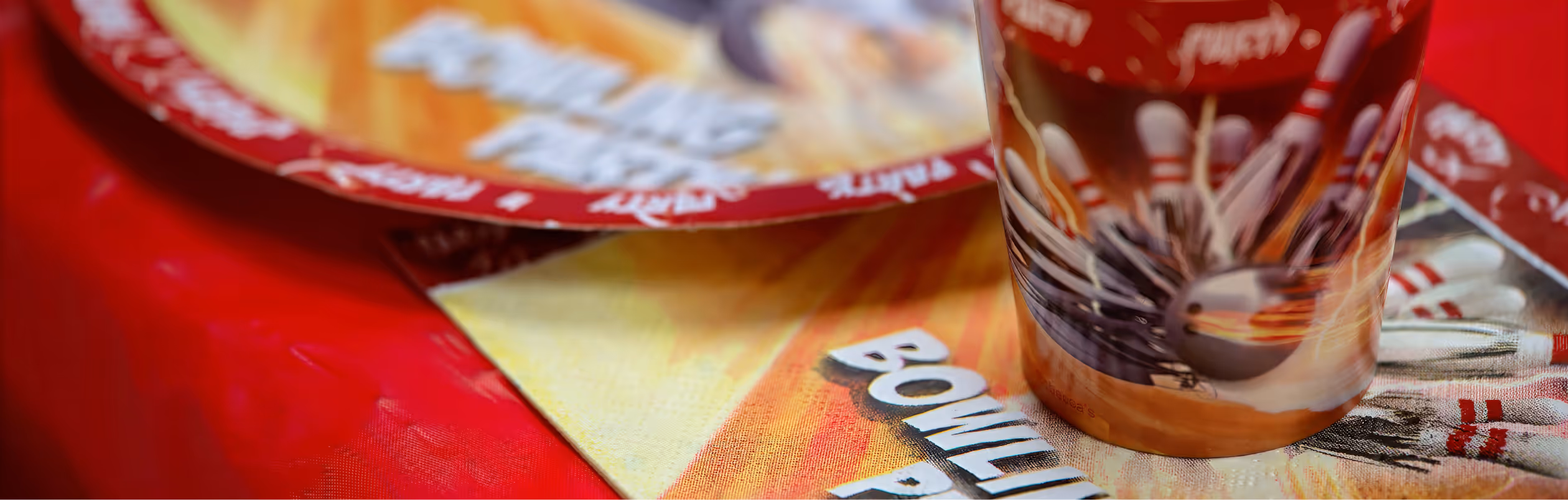Close-up of bowling-themed party plates and a cup on a red tablecloth.